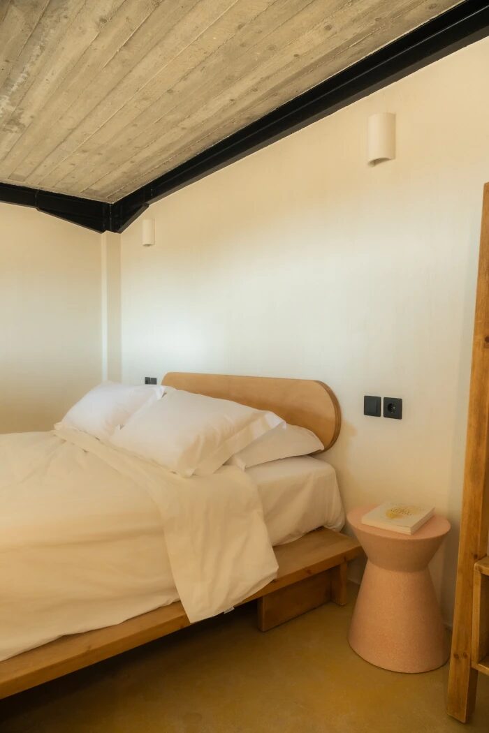 Chora View Suite bedroom — Cocomat double bed dressed in pure white linen, concrete ceiling and warm clay accents