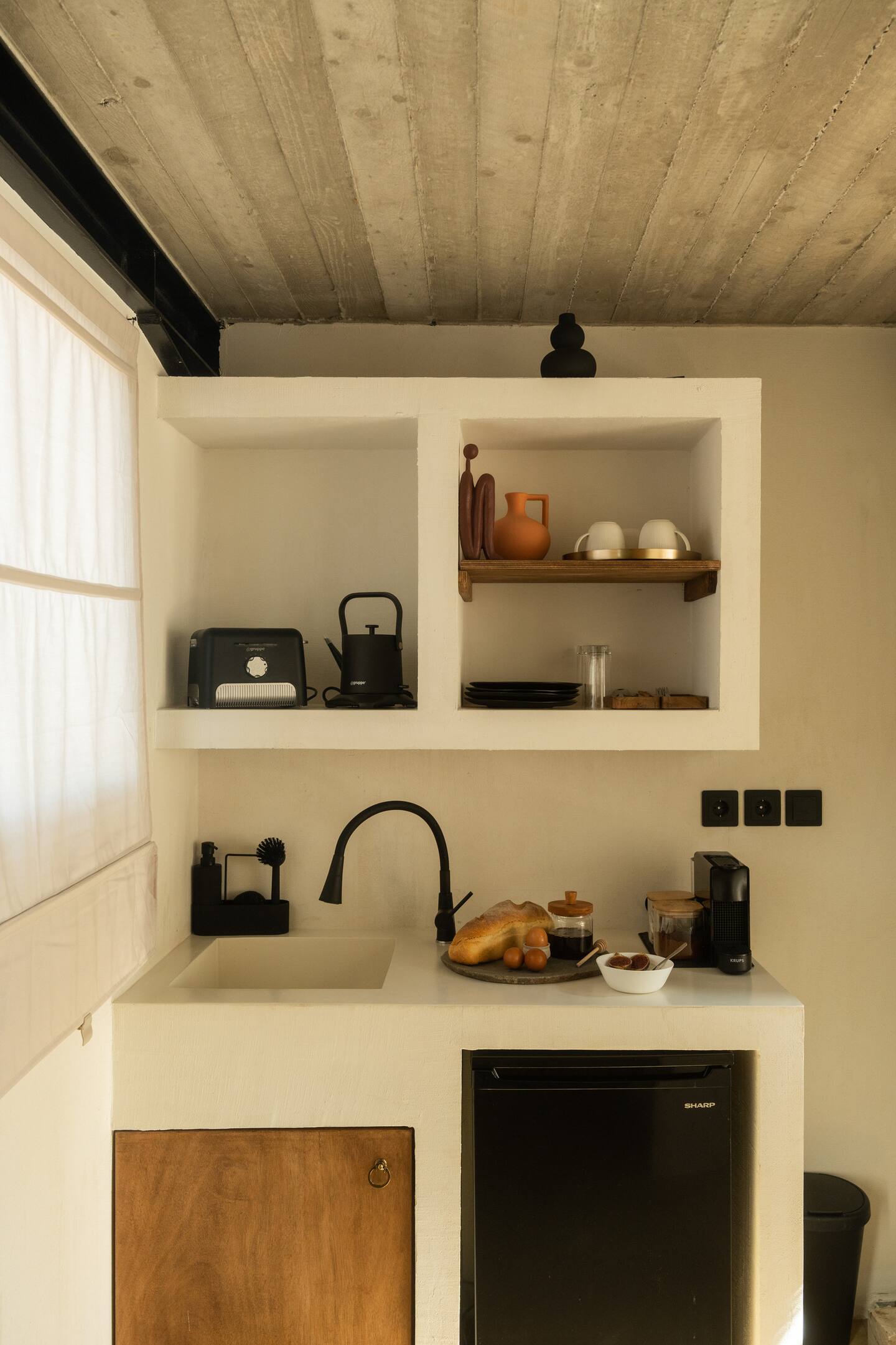Skyrian kitchenette detail — fresh bread, espresso machine, ceramic vessels and a small jar of honey in raking morning light