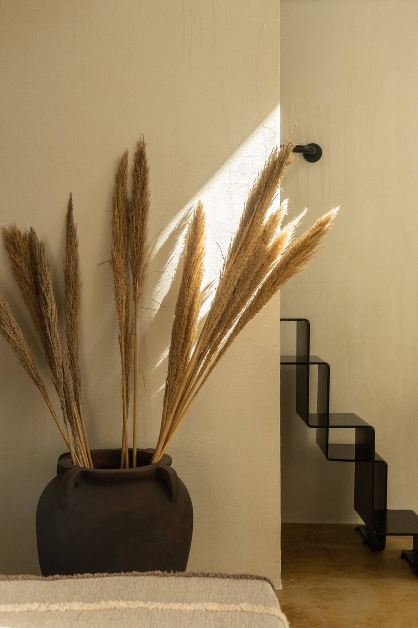 Detail — dried pampas grass in a dark ceramic urn beside black steel staircase