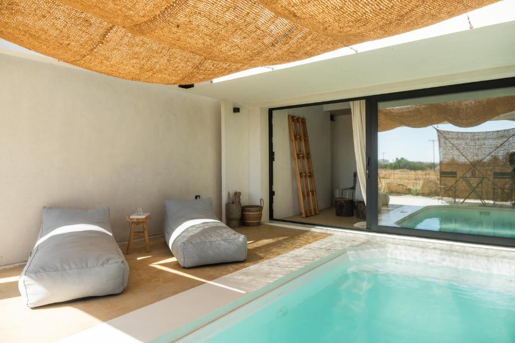 Sea View Suite — private pool with linen loungers under hand-woven jute canopy, looking through sliding doors into the airy interior and the second pool beyond, Skyros