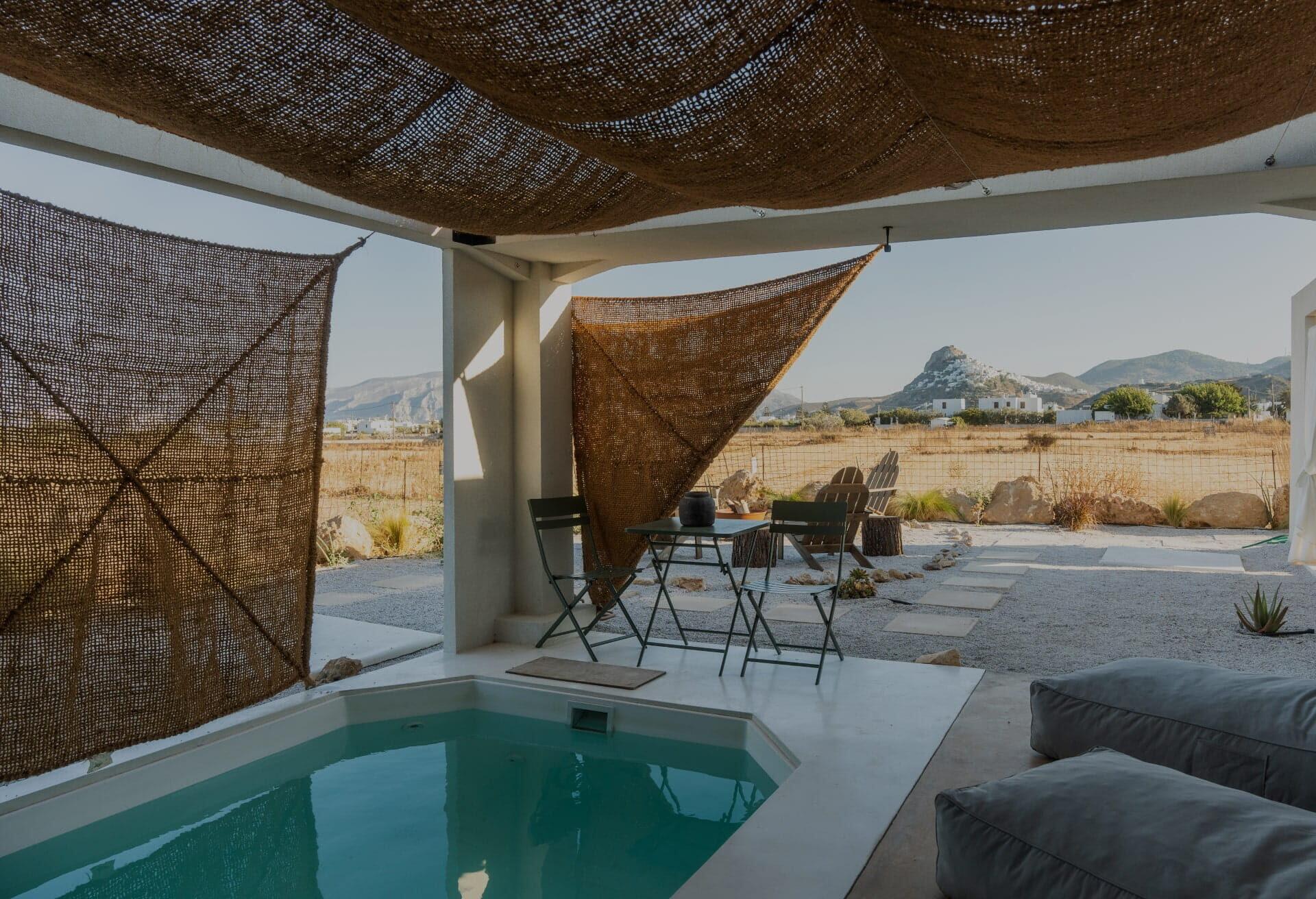 Chora View Suite — private pool under hand-woven jute canopy, with the whitewashed village of Chora rising on the hill in the distance, Skyros